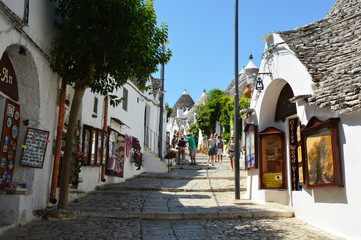 Beautiful street of Alberobello with trulli houses among green plants and flowers, main touristic district, Apulia region, Southern Italy