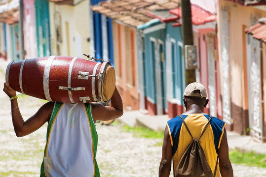 Salsa musician carrying a conga while walking in the streets of Trinidad Cuba with a friend