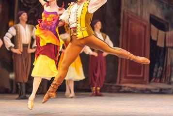 amusement, grace, dancing concept. ballet duet of male and female dancers dressed in bright multi colored costumes in yellow shades floating above the stage holding each other