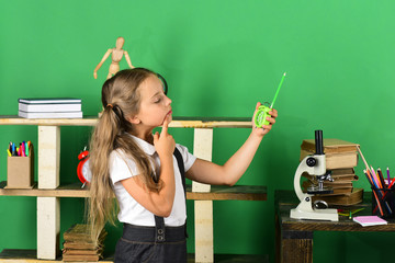 Kid and school supplies on green background. Girl holds clock