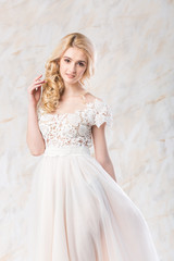Fototapeta na wymiar fashionable wedding dress, beautiful blonde model, bride hairstyle and makeup concept - perfect young woman in luxury white gown indoors on light background, lovely female posing in the studio