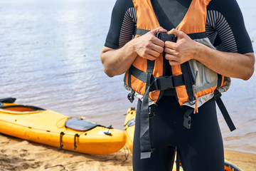  Young hiker wearing wetsuit putting on a life jacket before sailing on kayak 