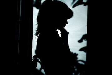 girl silhouette, sad woman standing near window in foliage and thinking how to solve the problem