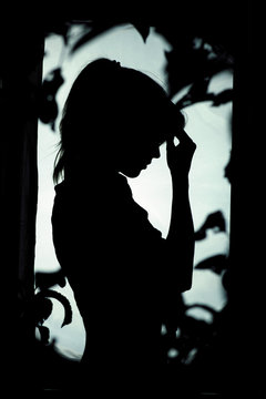 woman silhouette in depression, sad girl standing near window