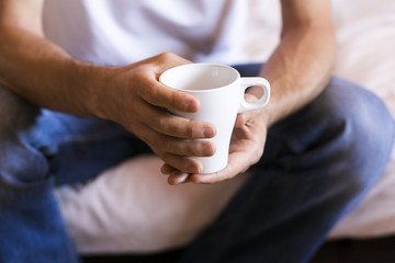 man hands holding a white cup of coffee in the morning. Sitting on the sofa. Daytime. Lifestyle