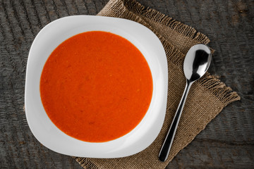 Gazpacho tomato soup in a white bowl with spoon on a towel on the background of wooden boards
