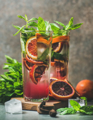 Blood orange citrus lemonade with mint and ice in tall glasses on wooden board over dark brown stone background. Refreshing summer drink concept
