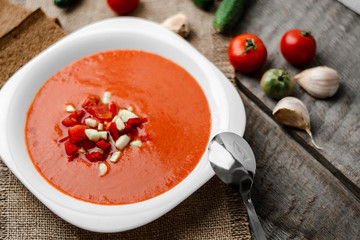 Gazpacho tomato soup in a white bowl spoon on a towel on the background of wooden boards