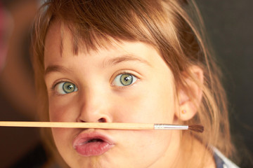 Little girl holding a brush with her lips