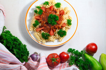 Vegetarian Vegetable pasta Fusilli with parsley, tomatoo and pepper in white plate on white wooden table. Top view