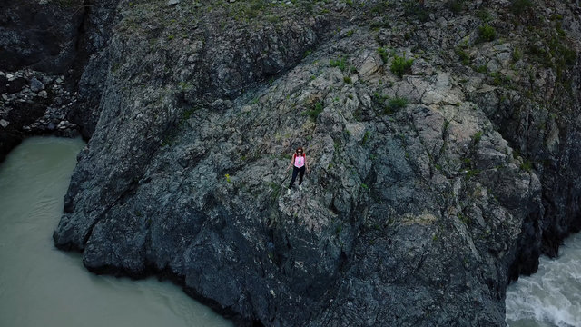 Aerial. woman traveler with backpack enjoying a stunning view standing on the edge of the cliff on a mountain river. Altai, Siberia. Aerial camera shot