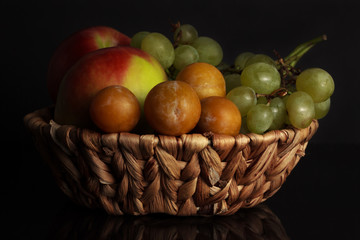Fruits of grapes, plums and an apple in a wicker basket