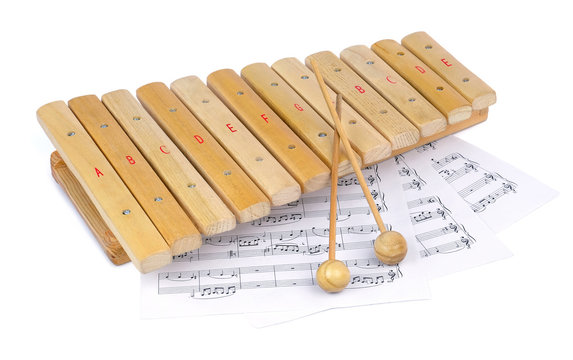 Small wooden xylophone and several sheets of paper with musical notes under it, isolated on a white background.