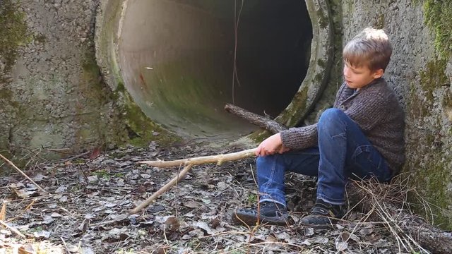 Little lonely kid has fun with long wooden stick outside in abandoned place in wood or forest. Real time full hd video footage.