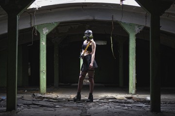 Beautiful, young girl post apocalypse girl stand in abandoned factory with gas mask and machine gun