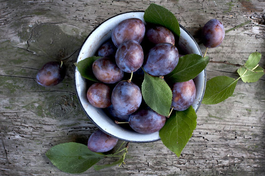 Ripe plums in plate on wooden background
