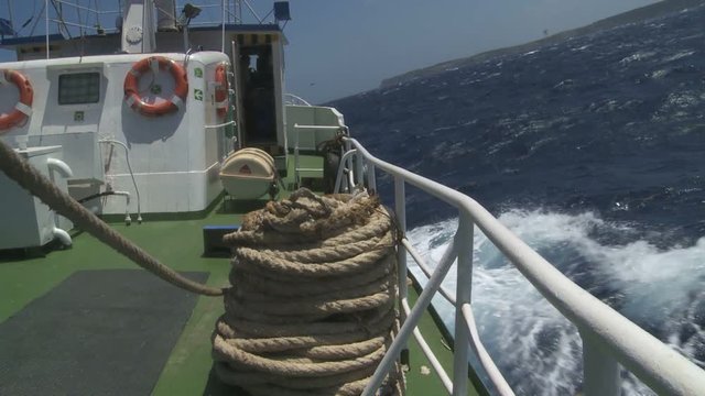 Fishing vessel balancing horizon in rough sea approacing to an island