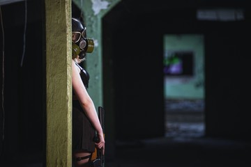 Beautiful, young girl post apocalypse girl stand in abandoned factory with gas mask and machine gun