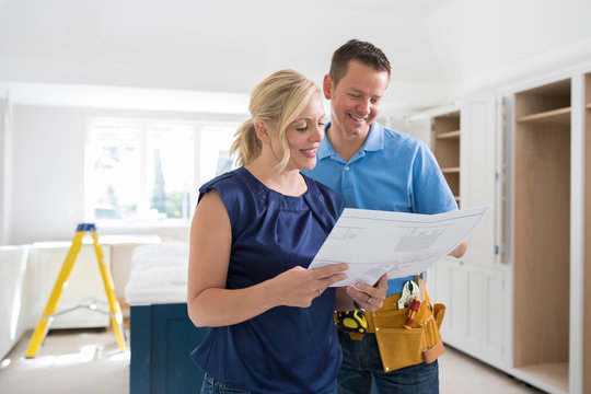 Woman With Carpenter Looking At Plans For New Kitchen