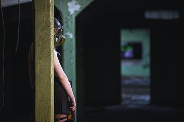 Beautiful, young girl post apocalypse girl stand in abandoned factory with gas mask and machine gun