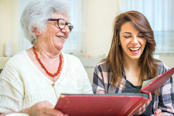 Grandmother and granddaughter looking at old photos at photo album.