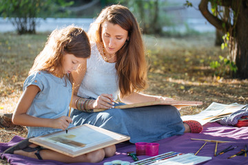 Woman with daughter drawing by watercolor paints at the park
