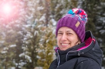 Portrait of Smiling Young Woman in Ski Outfit with Trees Covered in Snow in Background