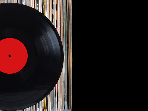 Black record with red label and pile of many close standing vinyl records in old color covers on left side on photo over black background studio shot front view closeup