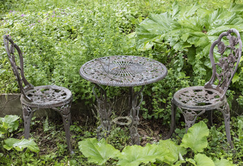 Deux chaises et une table dans le jardin entouré de feuillage vert.