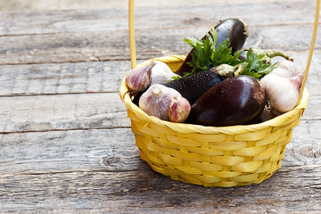 A wicker basket of vegetables eggplant garlic greens on wooden concrete background on the street. Selective focus. Copy space.