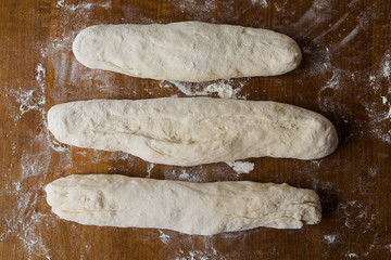 Three homemade French baguettes on wooden surface ready for rising