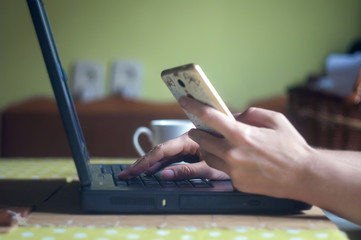Silhouette of young woman working from home using smart phone and notebook computer, woman's hands using smart phone in interior