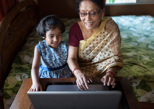 Girl and her grandmother having fun while using laptop