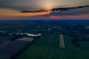 Beautiful panoramic aerial view of the valley with green fresh fields and meadow at sunset. Twilight above the village with a lake