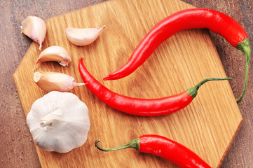 Hot chili peppers with the garlic bulb and cloves on a board