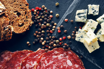 Roquefort slices with bread, sliced salami and peppercorns on the dark background