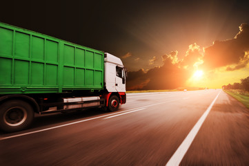 Truck driving fast with the container on the road against sky with sunset