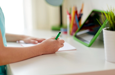 girl with tablet pc writing to notebook at home