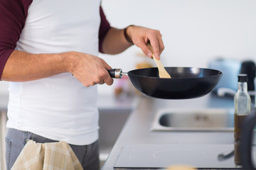 man with frying pan cooking food at home kitchen
