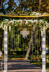 Arch for the wedding ceremony. Decorated with crystal chandelier and fresh flowers. Wedding decorations. The newlyweds.