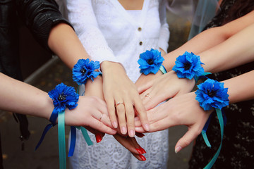 Hen-party before the wedding. Six female hands with blue flower boutonniere braceletes on wrist. Bride and her maids put their hands together.