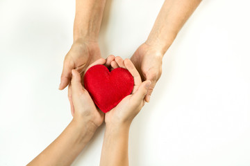 Felt red heart in childs and female hands on white background. View from above.