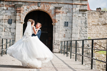 Handsome groom spinning his wife on his hands next to the old gates.