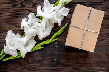 To wrap a gift. Box in kraft paper near flower gladiolus on dark wooden table top view