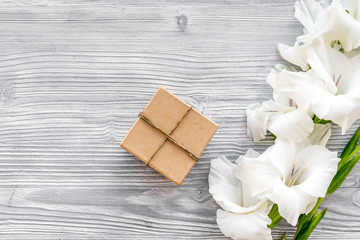 Celebration accessories. Box in kraft paper near flower gladiolus on light wooden table top view copyspace