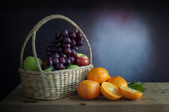 Grapes, apples and oranges  in a in wicker basket on a wooden table, still life style.