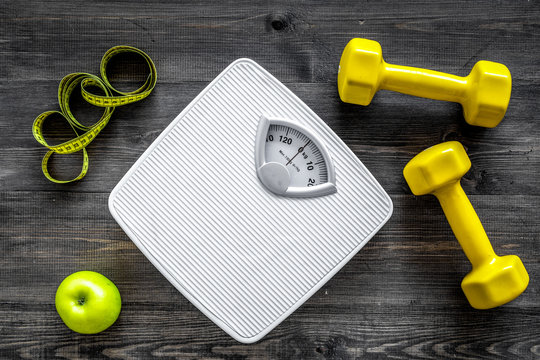 Sport and diet for losing weight. Bathroom scale, apple and dumbbell on wooden background top view