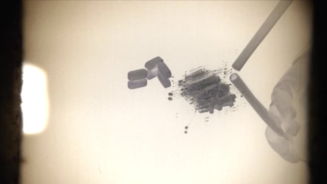 Fake 8mm amateur film: inhaling (snorting) cocaine on the mirror with a credit card. White pills lying nearby. Inverted colors, close-up view. Crime, abuse, drugs, social issues.
