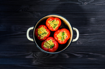 Four red stuffed peppers in a yellow saucepan on dark rustic kitchen table background, top view. Cooking process