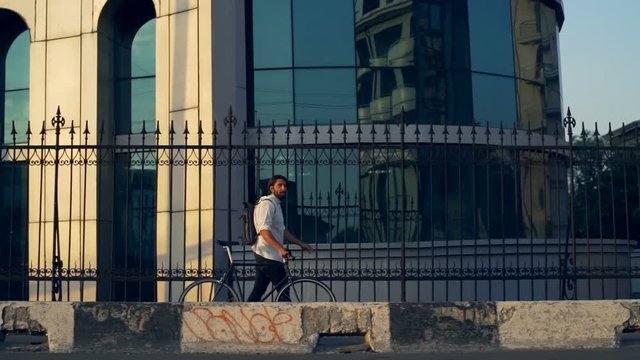 Young man walking with his bike in fornt of a big building slow motion